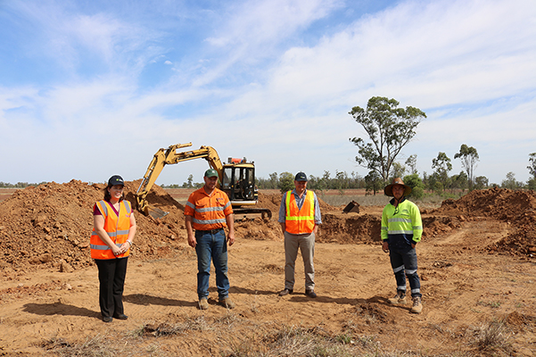 Four people stand in front of a pit in the earth, behind that is digging machinery.