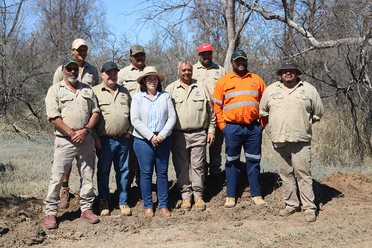 A group of people dressed in khaki utility clothing and high visibility utility clothing stand in bushland.