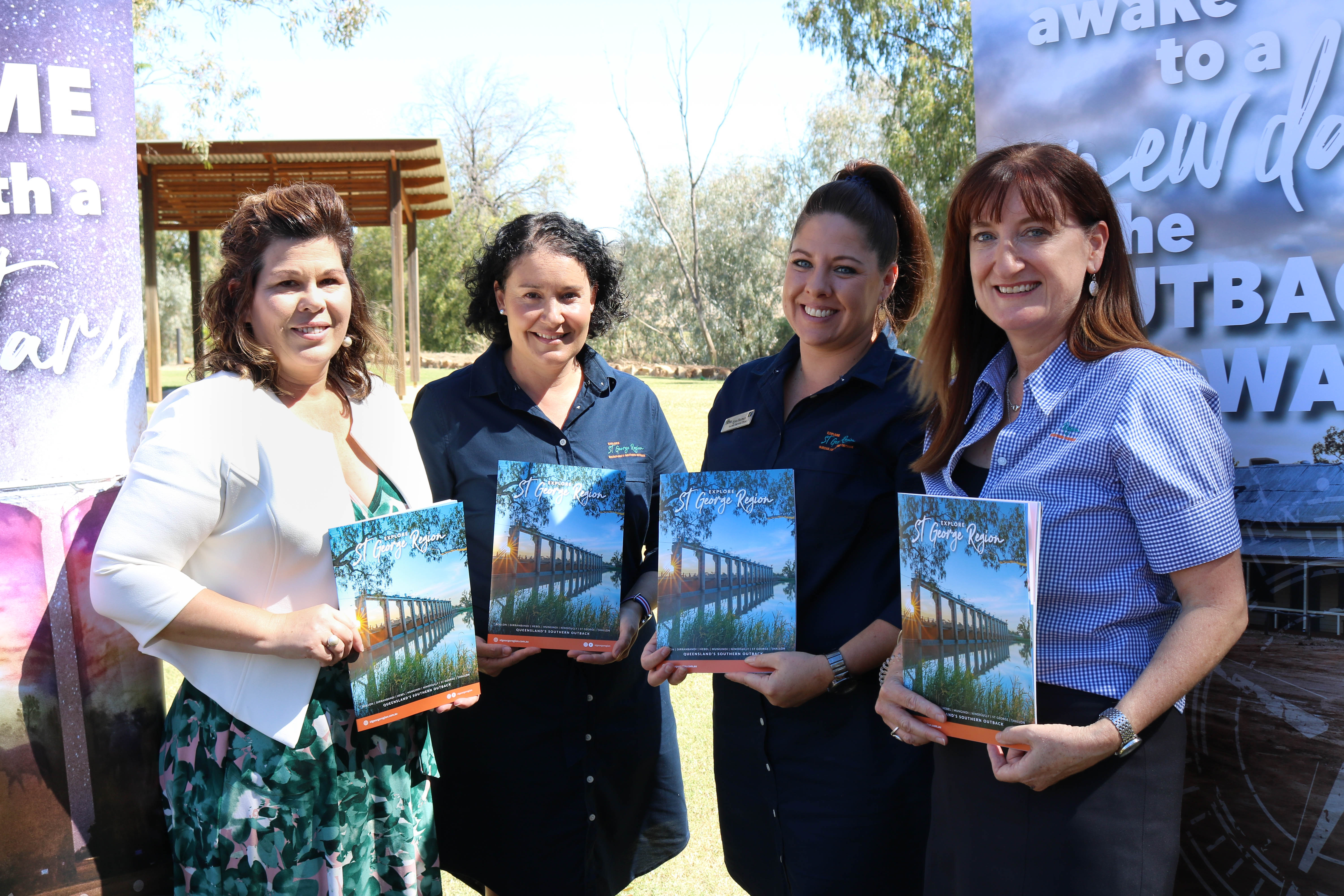 Four women stand together, smiling while holding visitor information brochures.