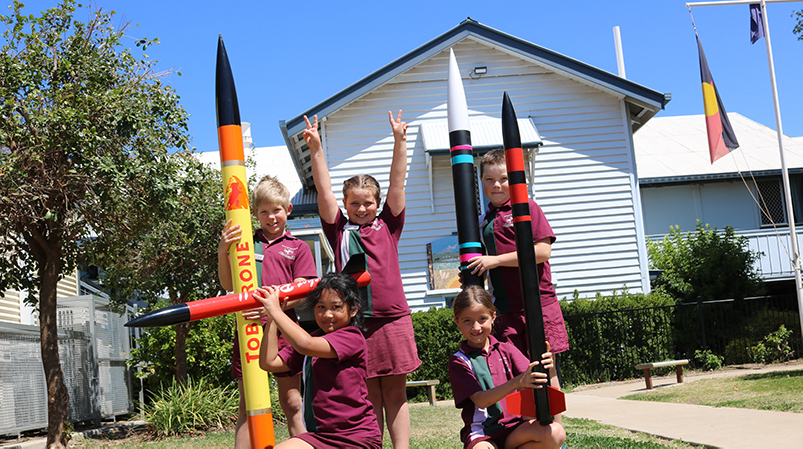 Five school children smile at the camera, they are holding model rockets.
